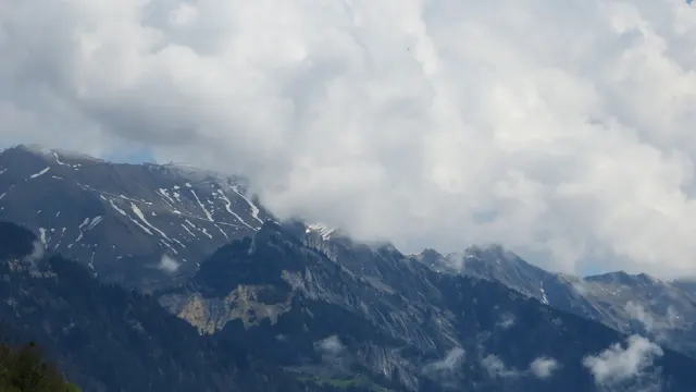 Thick clouds wrap around a dark mountain ridge streaked with snow.