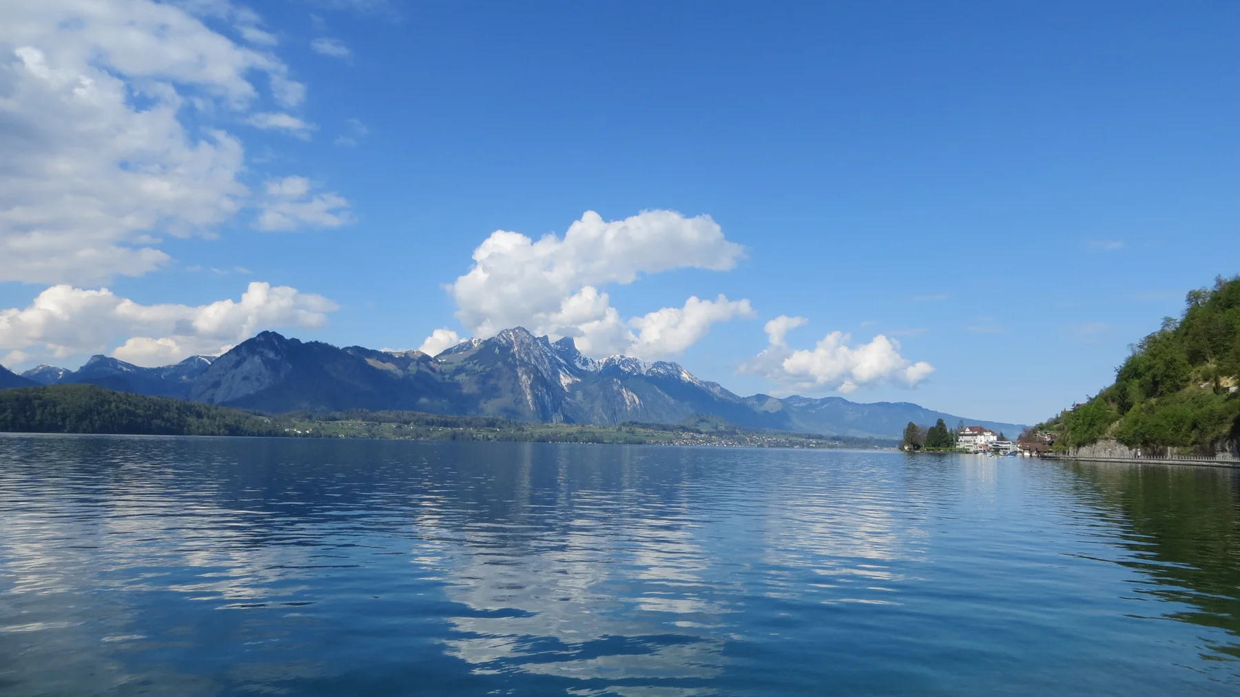 Distant mountains and white clouds reflect across the wide blue lake.