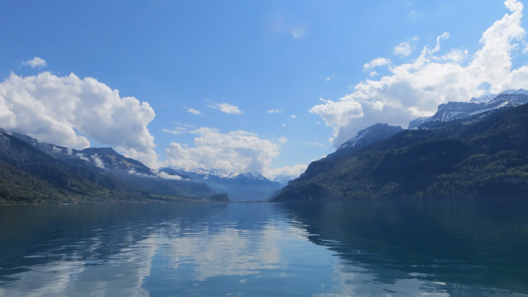 White clouds and mountain slopes mirror themselves along a narrow lake.