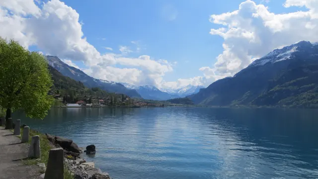 Stone posts line a lakeside path overlooking mountains and their reflection.