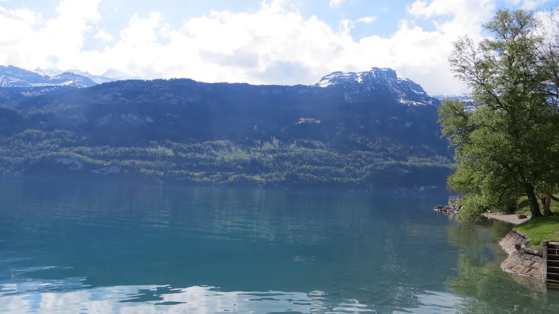 A mountain ridge and its reflection fill the lake beside a tree-lined stone shore.