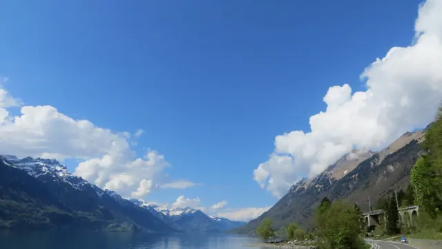 Blue sky opens between white clouds above a lake enclosed by steep mountains.
