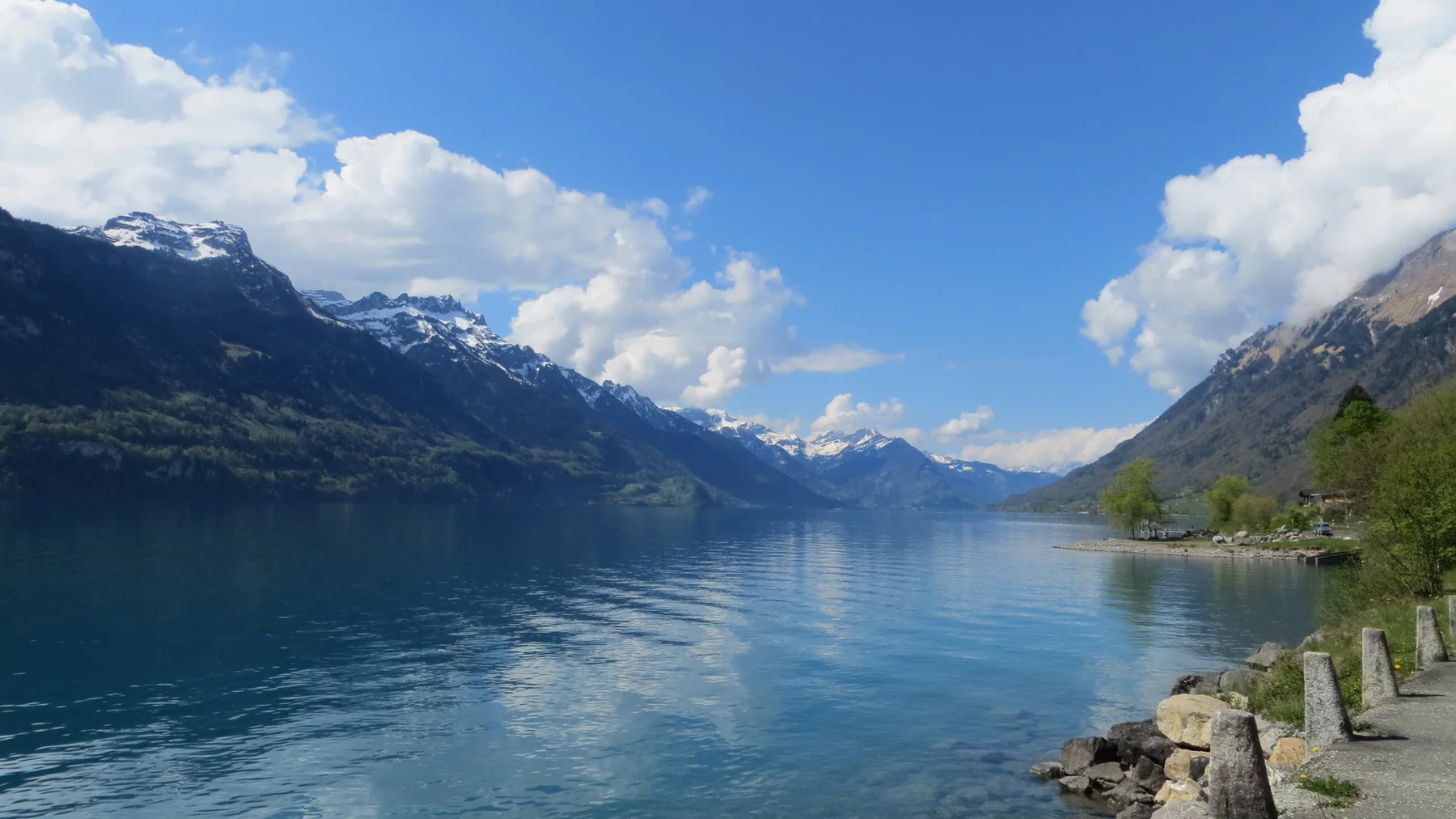 A long blue lake reflects white clouds between steep mountain walls.