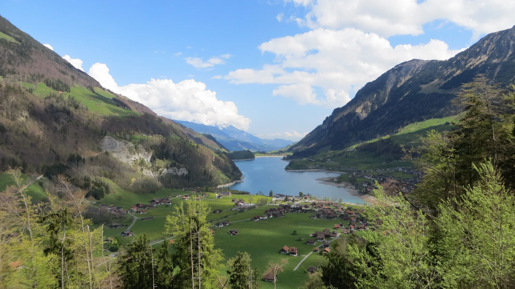 Green fields and scattered roofs spread toward a narrow mountain lake.