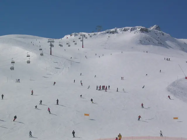 Small skiers spread across a wide snowy slope beneath ski lifts and a rocky crest.