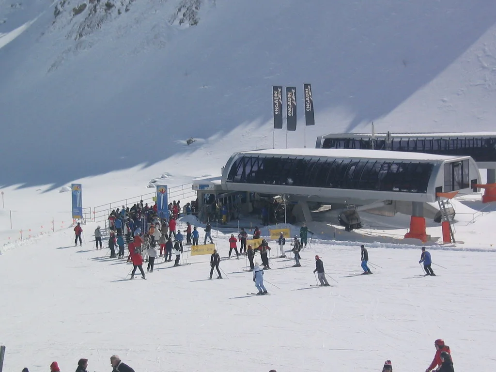 Skiers gather beside a lift station at the foot of a snow-covered slope.