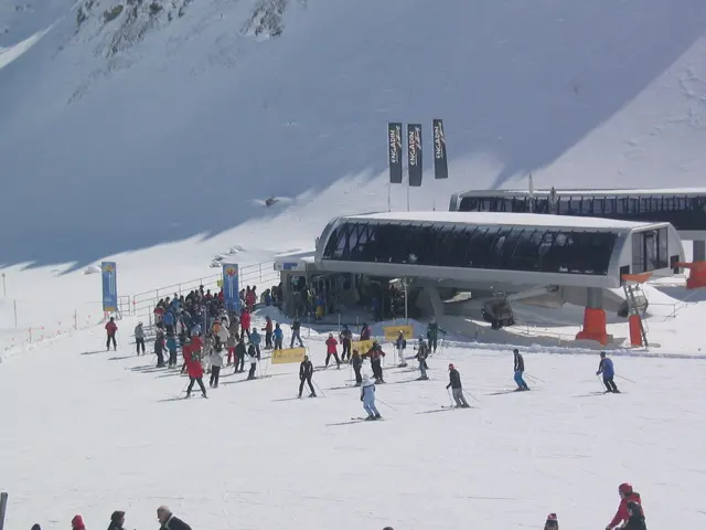 Skiers gather beside a lift station at the foot of a snow-covered slope.