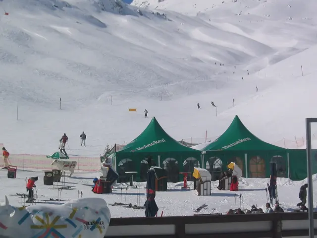 Green event tents and visitors stand beside a broad snowy ski slope.