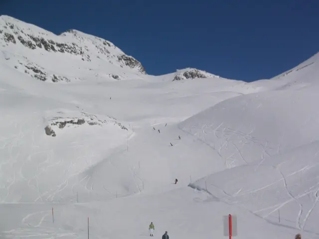 Snow-covered slopes curve below rocky peaks beneath a clear blue sky.