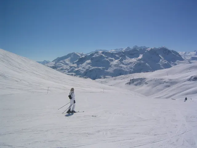 A skier crosses an open white slope with a distant mountain range behind.
