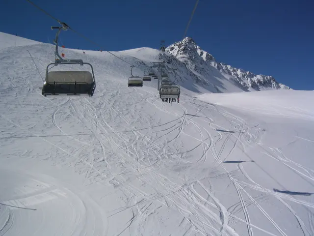 A chairlift passes above tracked snow toward a pointed mountain peak.