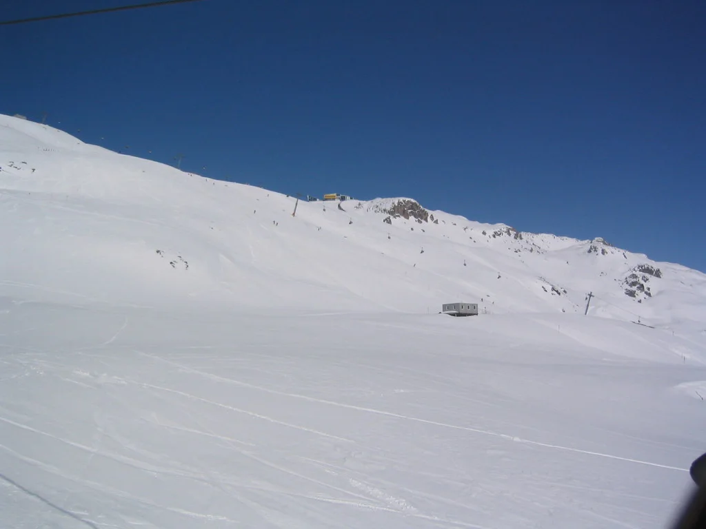 A wide snowfield curves below a low rocky ridge and deep blue sky.
