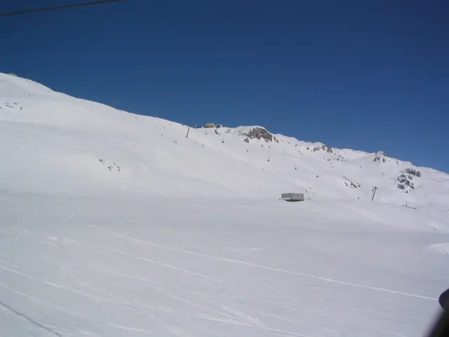 A wide snowfield curves below a low rocky ridge and deep blue sky.
