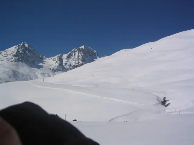 Two rugged snowy peaks rise beyond a smooth white slope with a dark foreground edge.