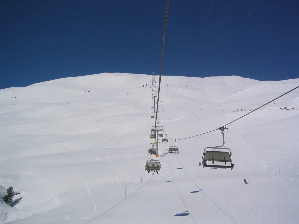 A line of chairlift towers climbs a snow-covered slope beneath clear blue sky.