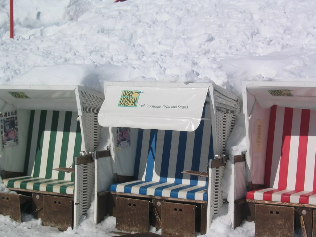 Green, blue and red striped hooded seats stand together against a bank of snow.