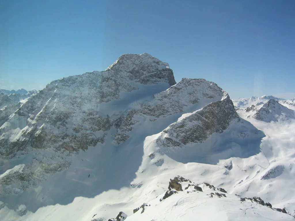 A rugged rock summit rises above deep snow and distant mountain peaks.