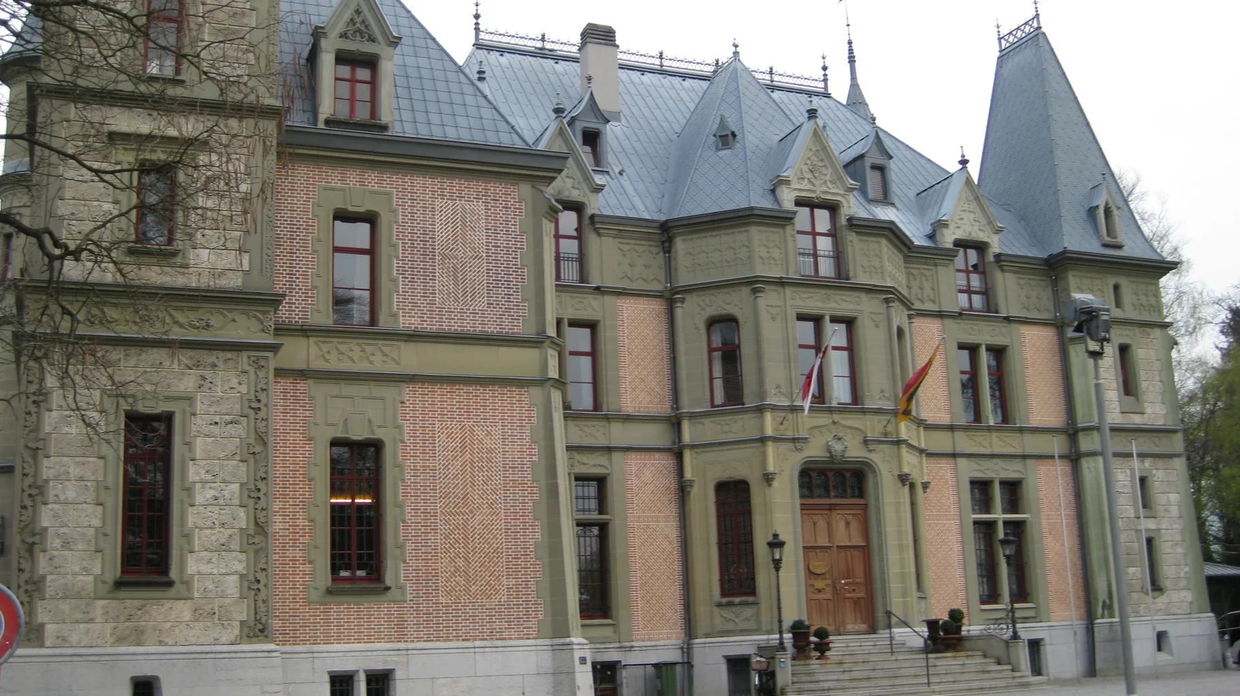 A carved entrance and tall windows punctuate a facade beneath steep slate-colored roofs.