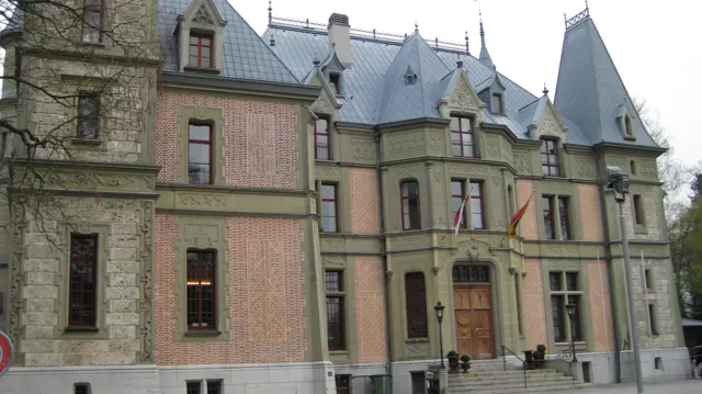 A carved entrance and tall windows punctuate a facade beneath steep slate-colored roofs.