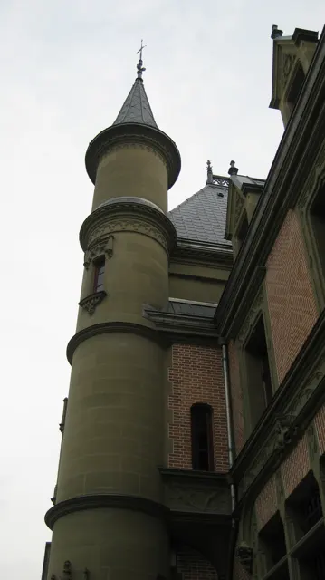 A narrow round tower rises beside a brick facade against a pale sky.