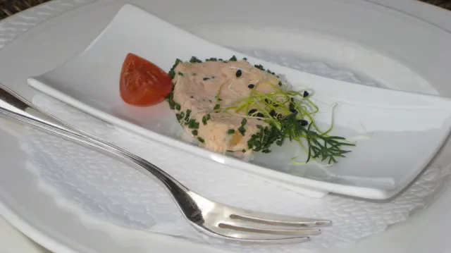 A small plated starter is garnished with herbs and a tomato wedge beside silver cutlery.