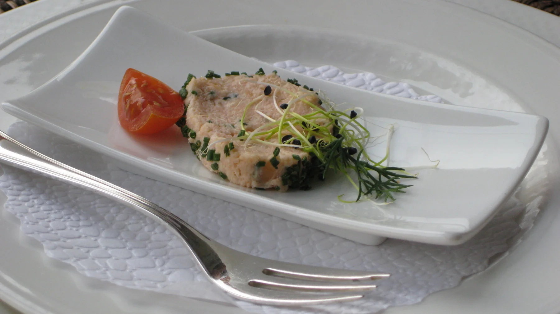 A molded starter with green herbs and a tomato wedge rests on a small white plate.