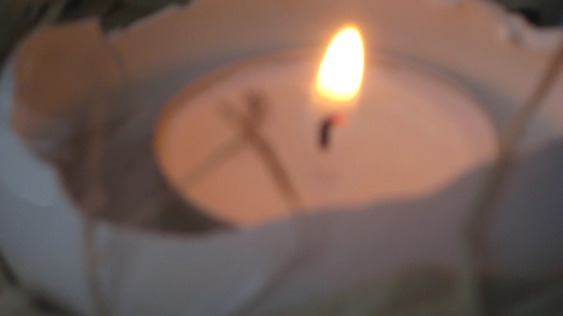 A candle flame glows above pale wax in a softly focused holder.