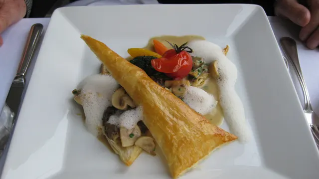 A long golden crisp tops a plated dish with vegetables and a small red tomato.
