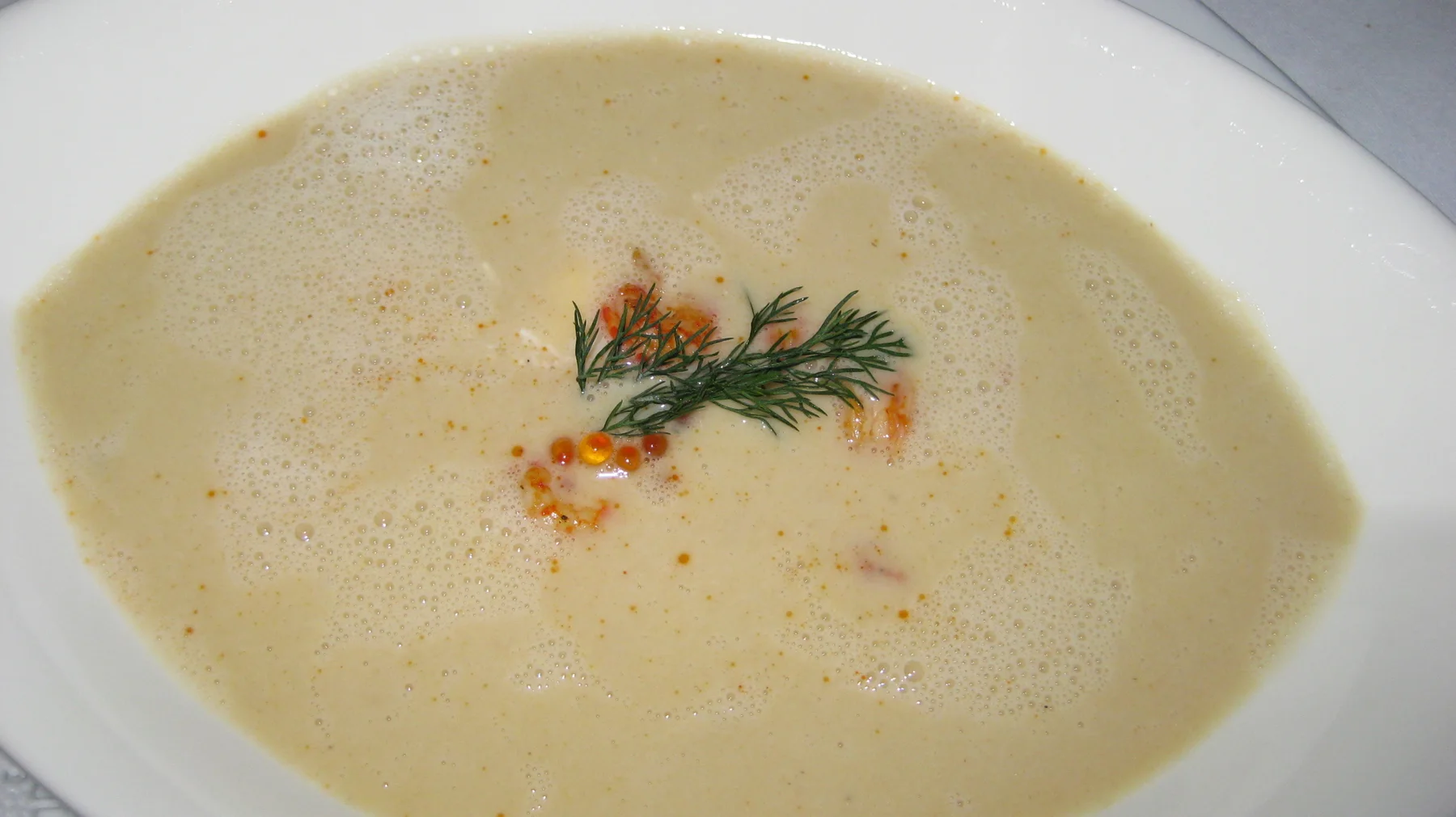A pale creamy soup is finished with a small green herb garnish in a white bowl.