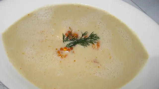 A pale creamy soup is finished with a small green herb garnish in a white bowl.