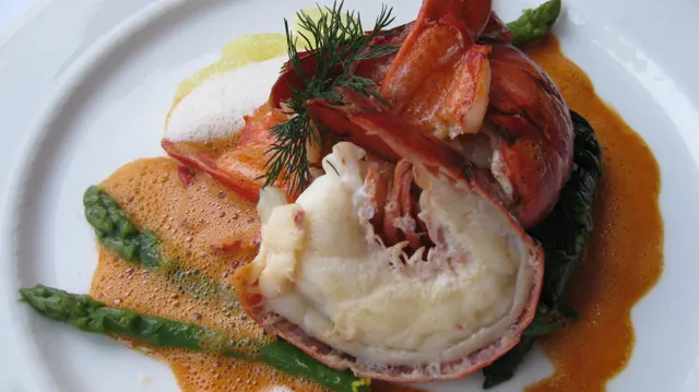 Red-shelled seafood is served with green asparagus and orange sauce on a white plate.