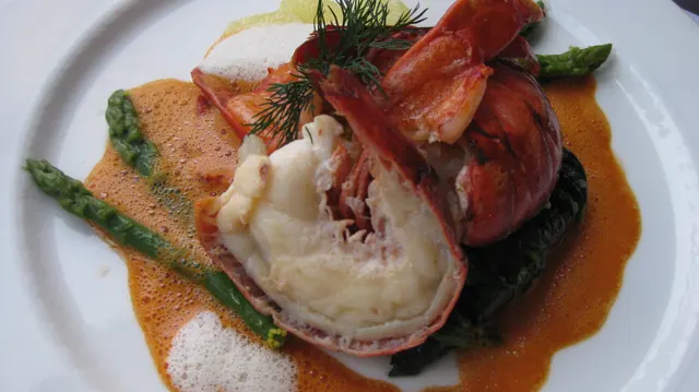Shellfish, asparagus and a foamy orange sauce fill a close view of a white plate.