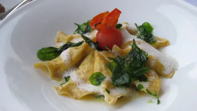 Leafy greens and a tomato garnish top pasta dusted with a pale grated topping.
