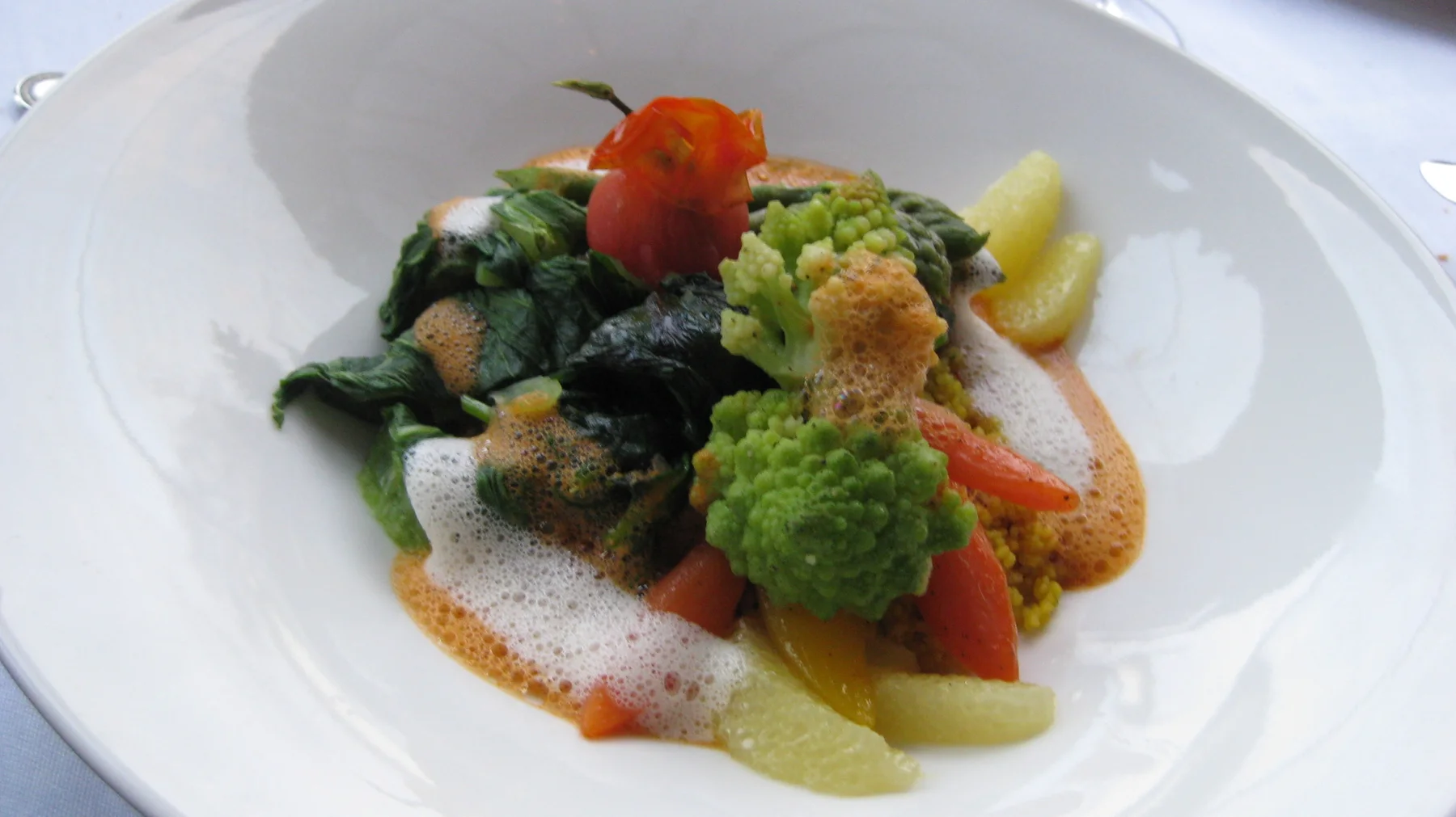 Green florets and colorful vegetable pieces are arranged with sauce in a white bowl.