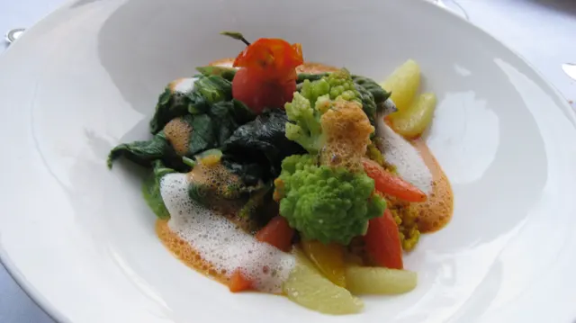 Green florets and colorful vegetable pieces are arranged with sauce in a white bowl.