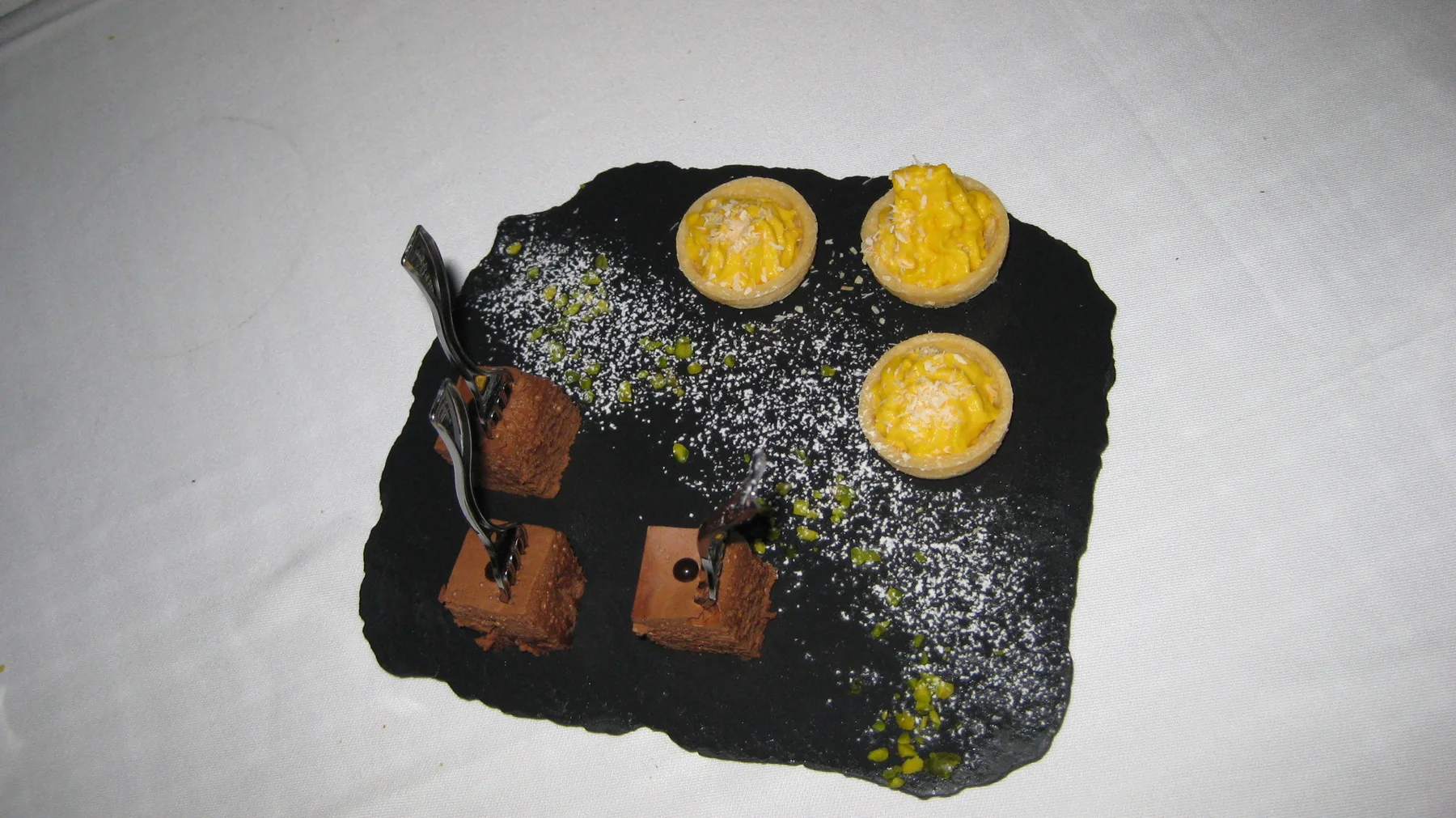 Small chocolate-colored and yellow sweets sit on a black slate dusted with a pale topping.