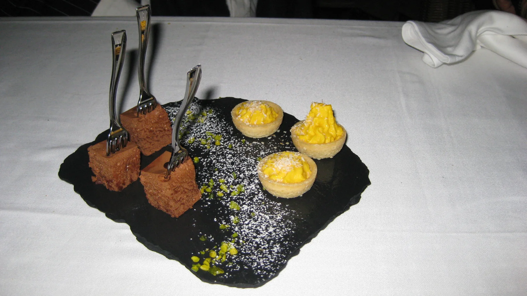 An assortment of small sweets is arranged on a dark slate on a white tablecloth.