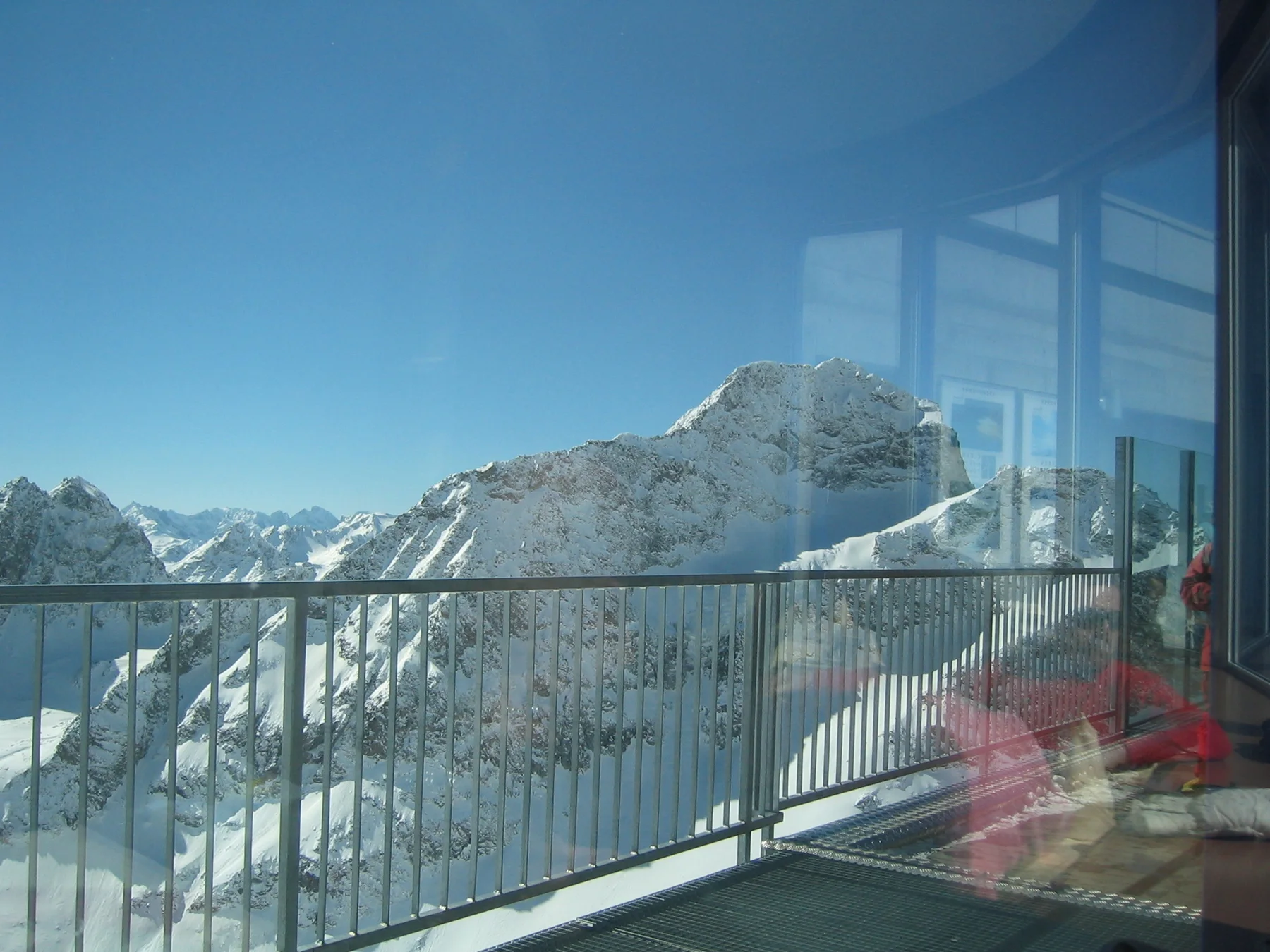 Window reflections overlap a balcony railing and snow-covered mountain peaks.