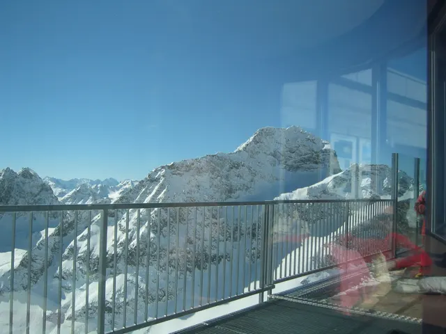 Window reflections overlap a balcony railing and snow-covered mountain peaks.