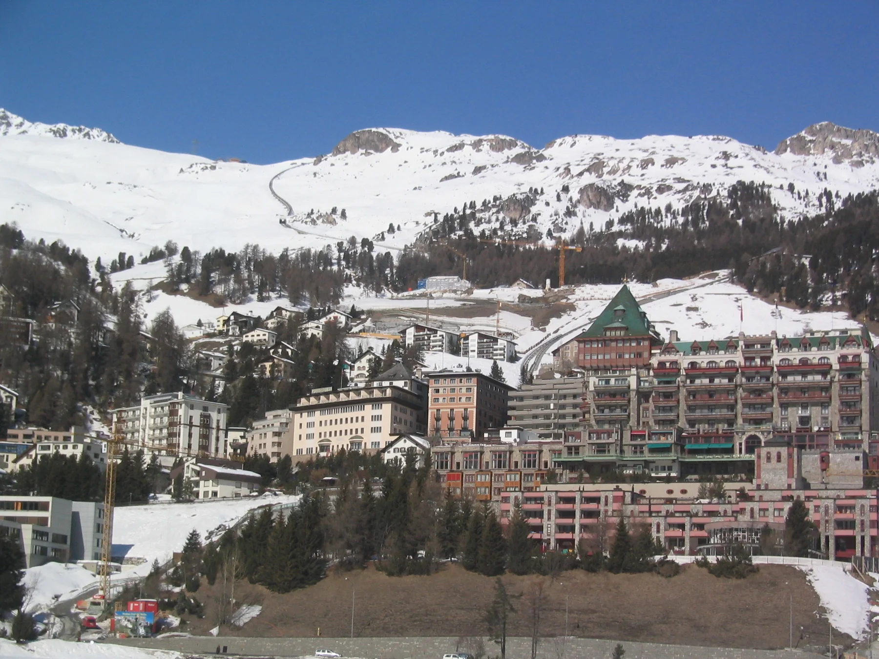 Large, ornate buildings stand below a snowy hillside and scattered trees.