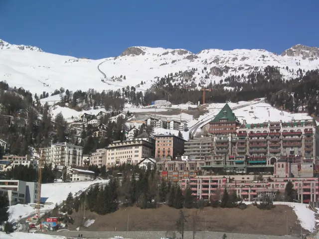 Large, ornate buildings stand below a snowy hillside and scattered trees.