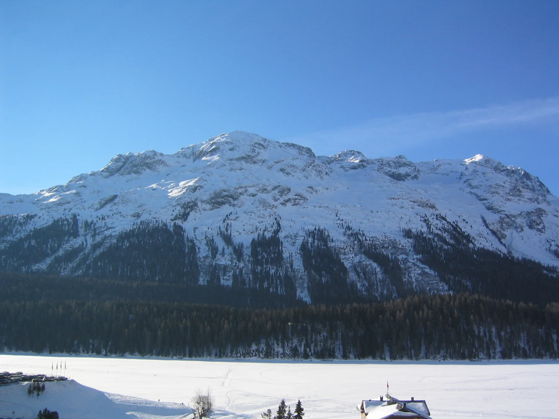 A broad snowy mountain rises beyond dark forest and a white valley floor.