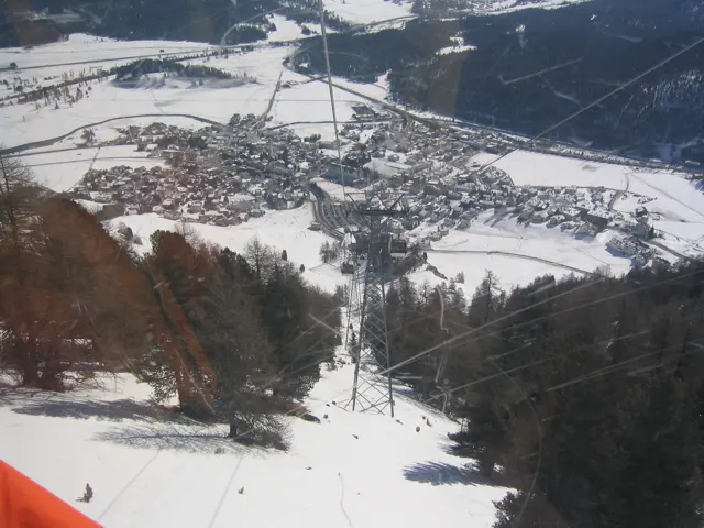 A steep snowy slope and lift line lead toward buildings spread across a winter valley.