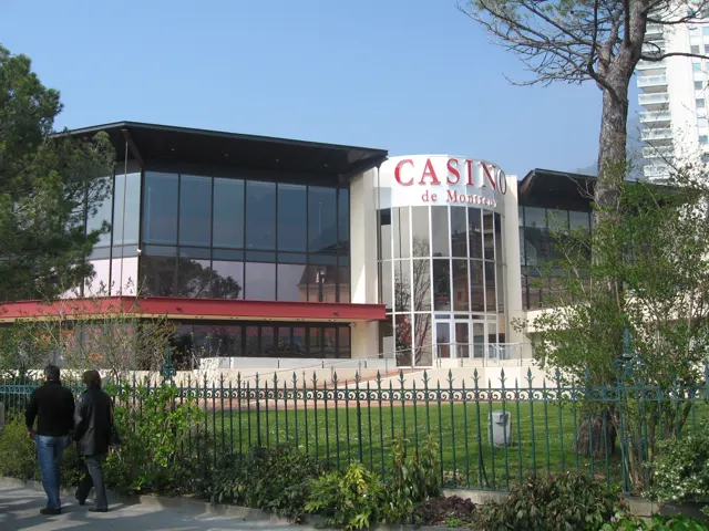 A glass-fronted casino building stands behind a garden and iron fence.