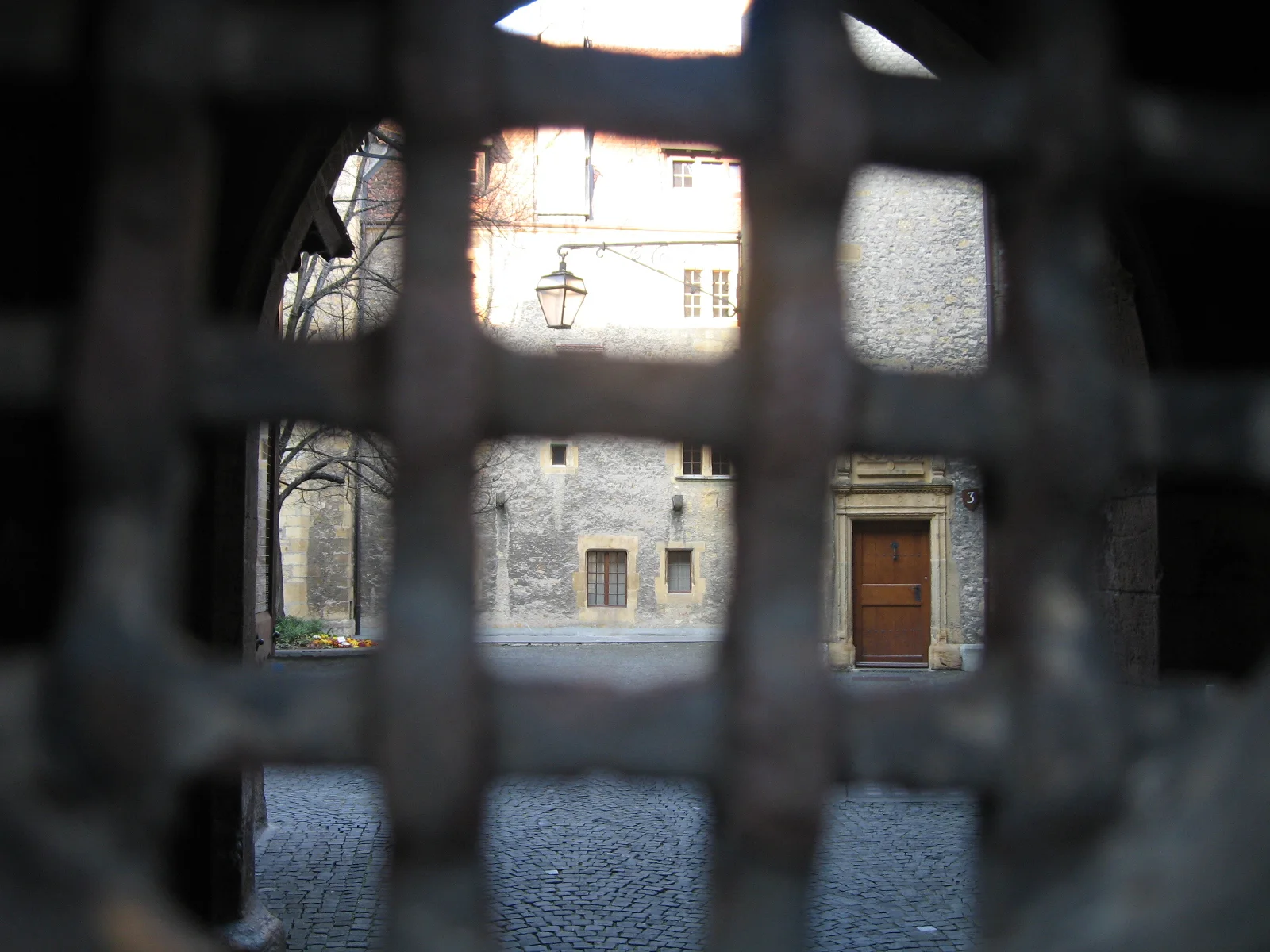A dark metal grille frames a view of a paved courtyard and building entrance.