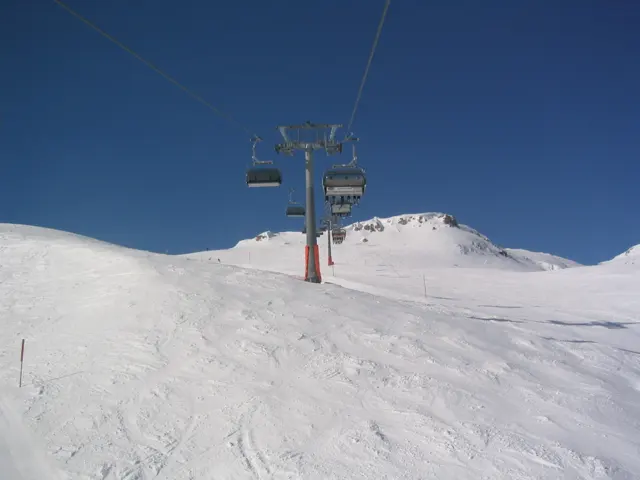Chairlift towers rise above a tracked snowy slope beneath a clear blue sky.