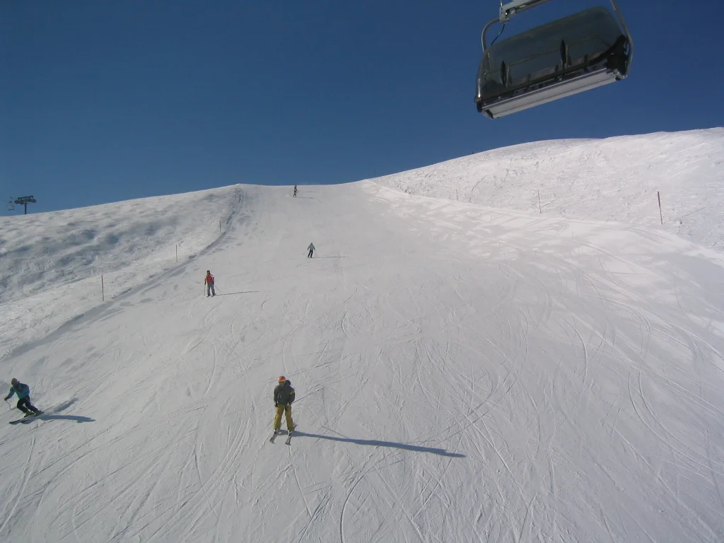 Skiers cross a white slope beneath a chairlift seat.