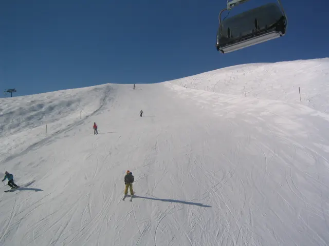 Skiers cross a white slope beneath a chairlift seat.