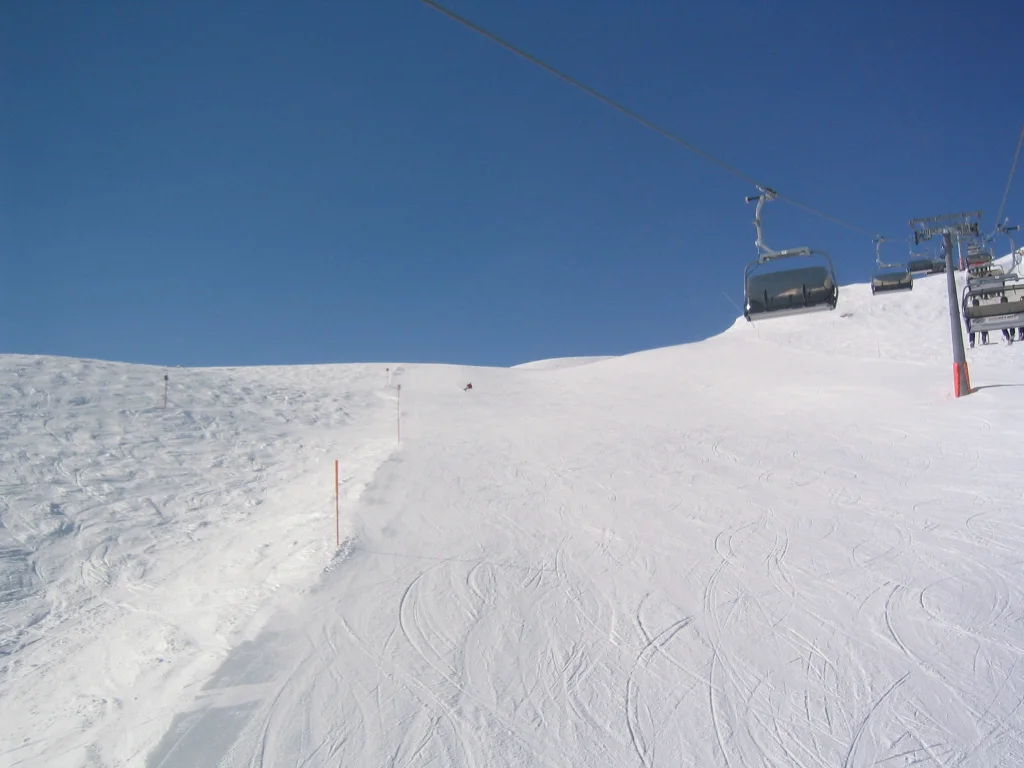 A snowy track leads uphill toward a chairlift at the crest.