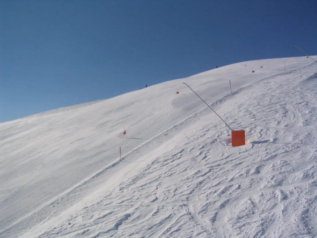 Ski tracks cross a sunlit slope beside an orange piste marker.